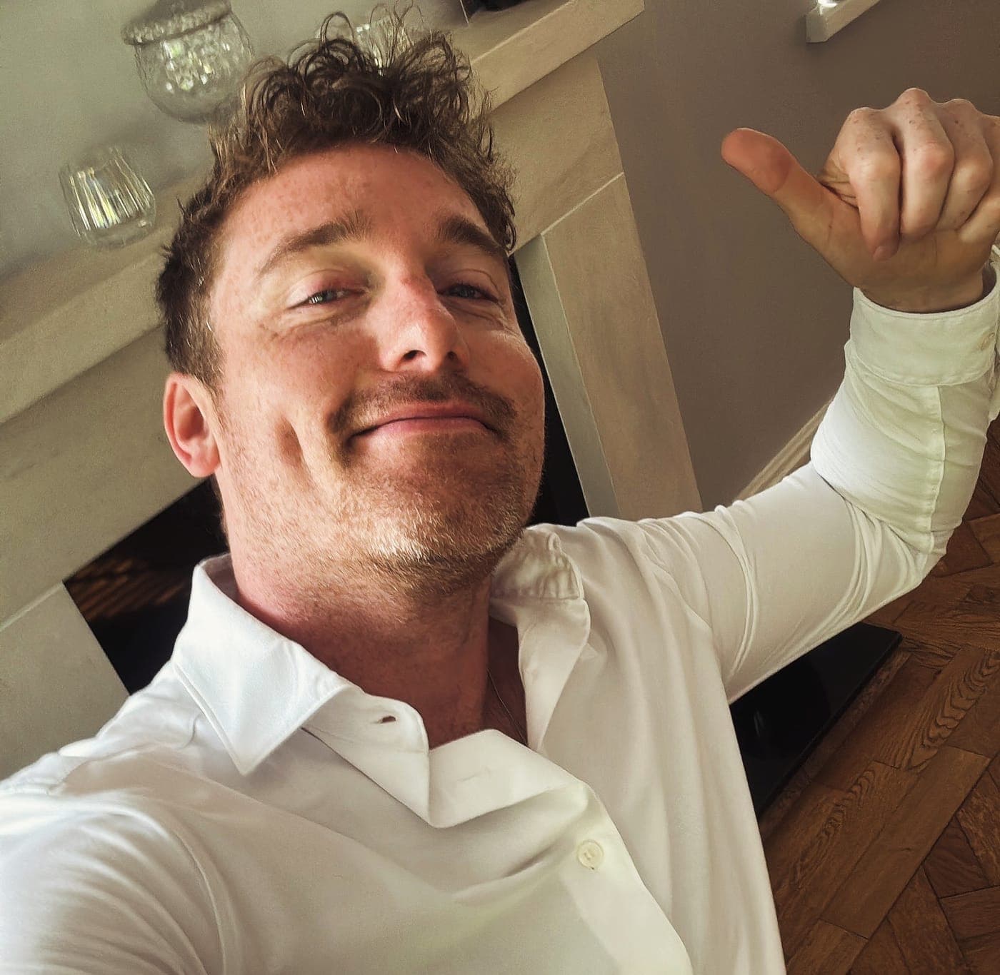 Christopher Adams in a white shirt, smirking, giving a thumbs up