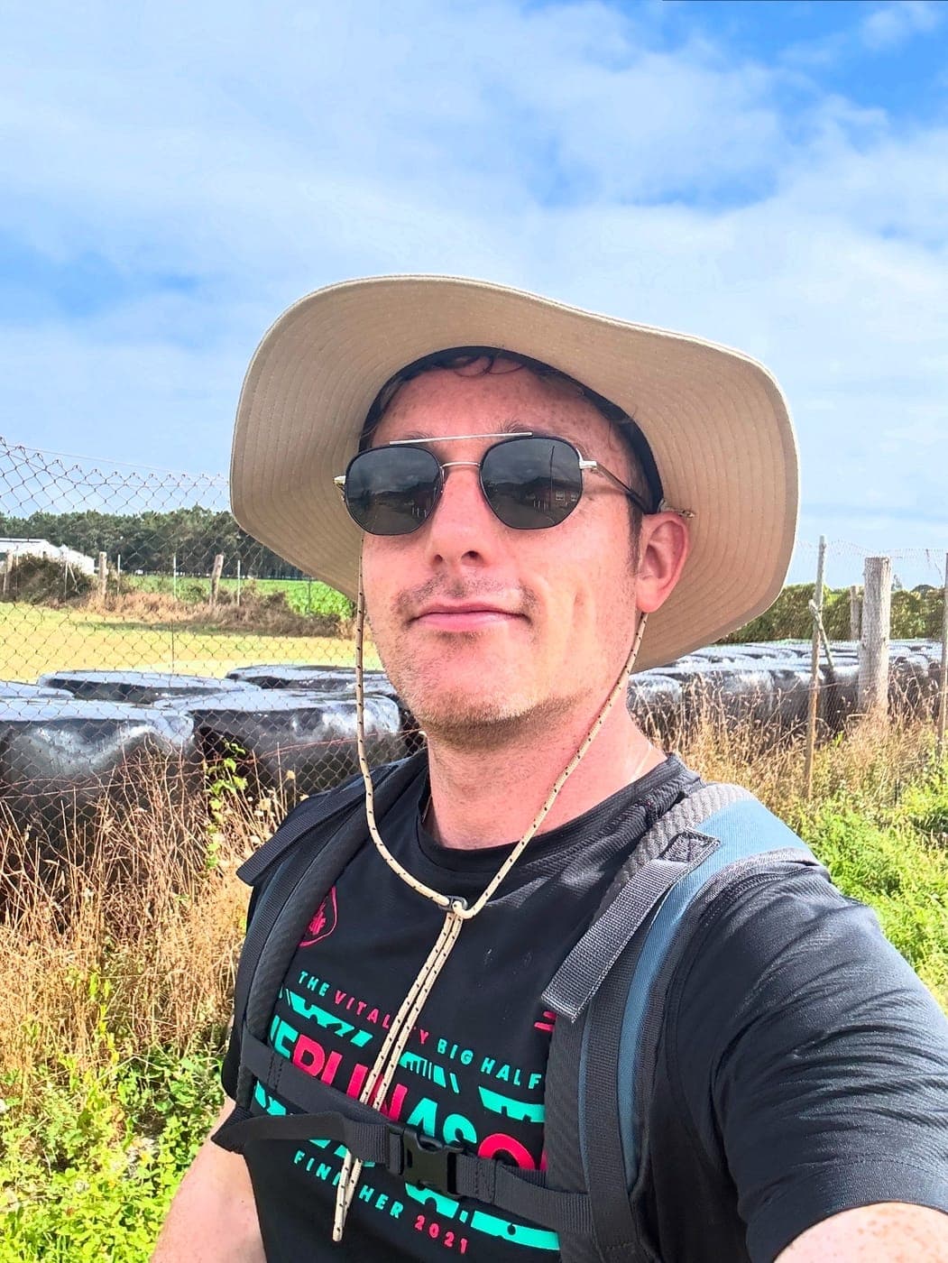 Christopher Adams in a sun hat and sunglasses on a walk through farmland