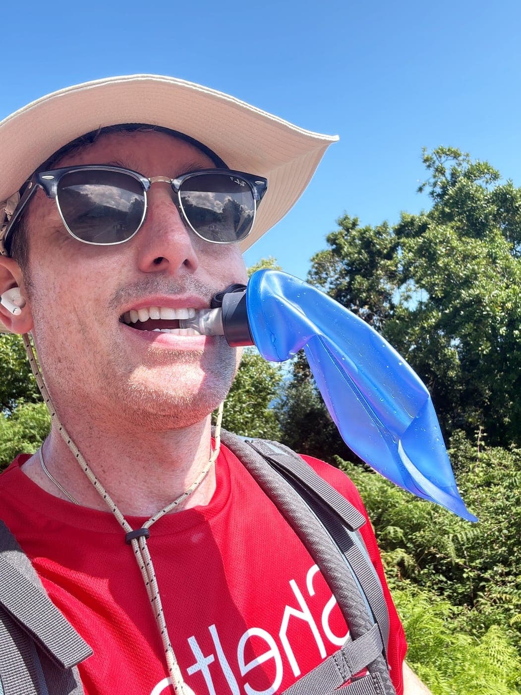 Christopher Adams in a sun hat drinking from a water bottle on a hike