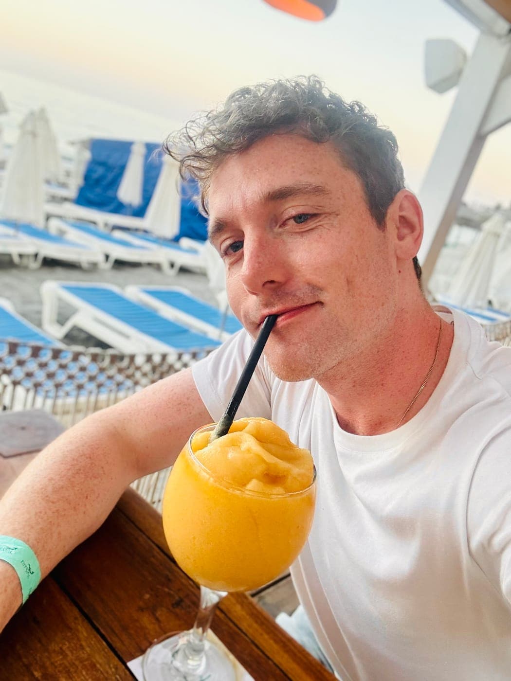 Christopher Adams with a mango slush and a straw, sun loungers behind