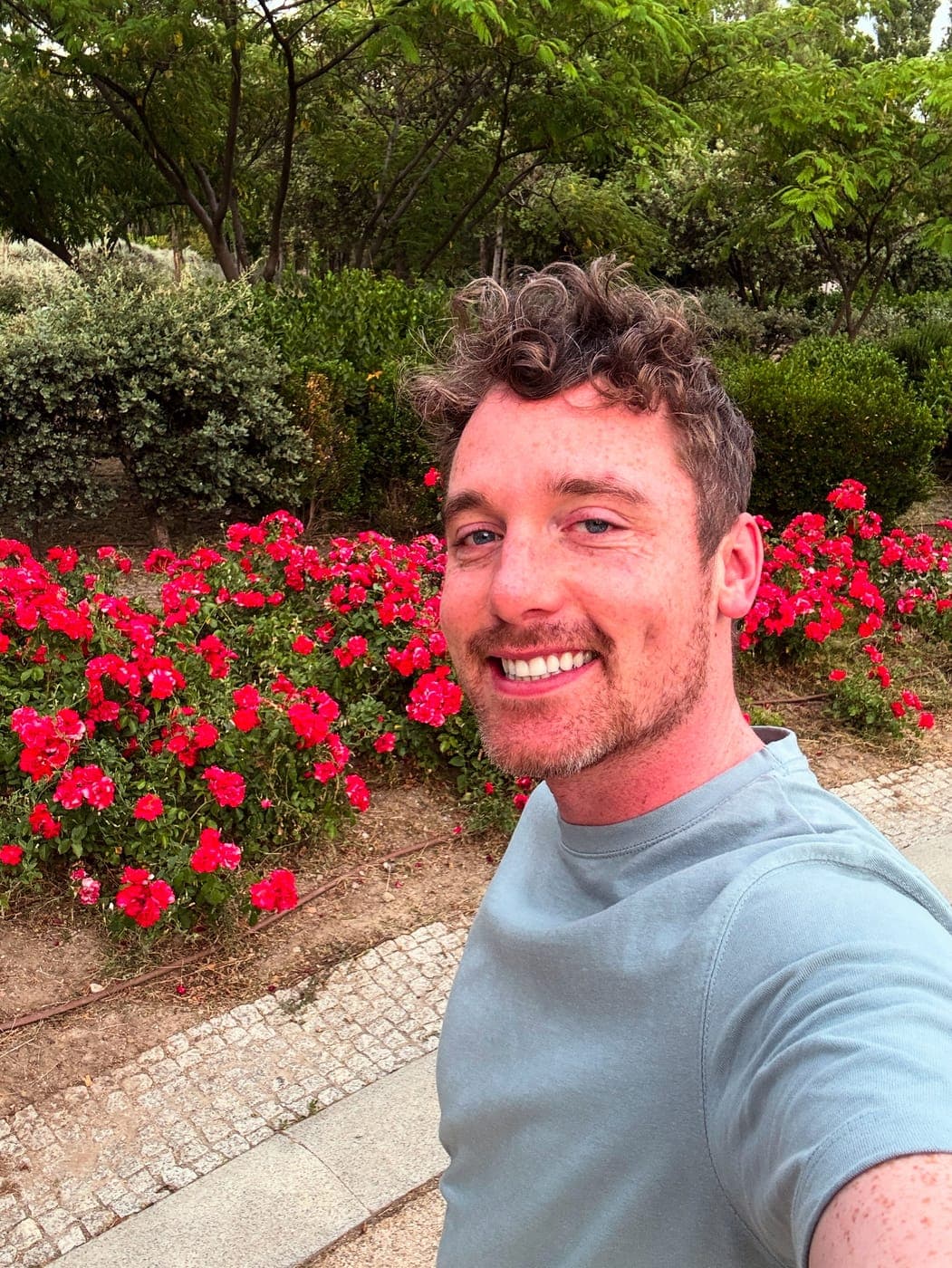 Christopher Adams smiling in front of a bed of red roses