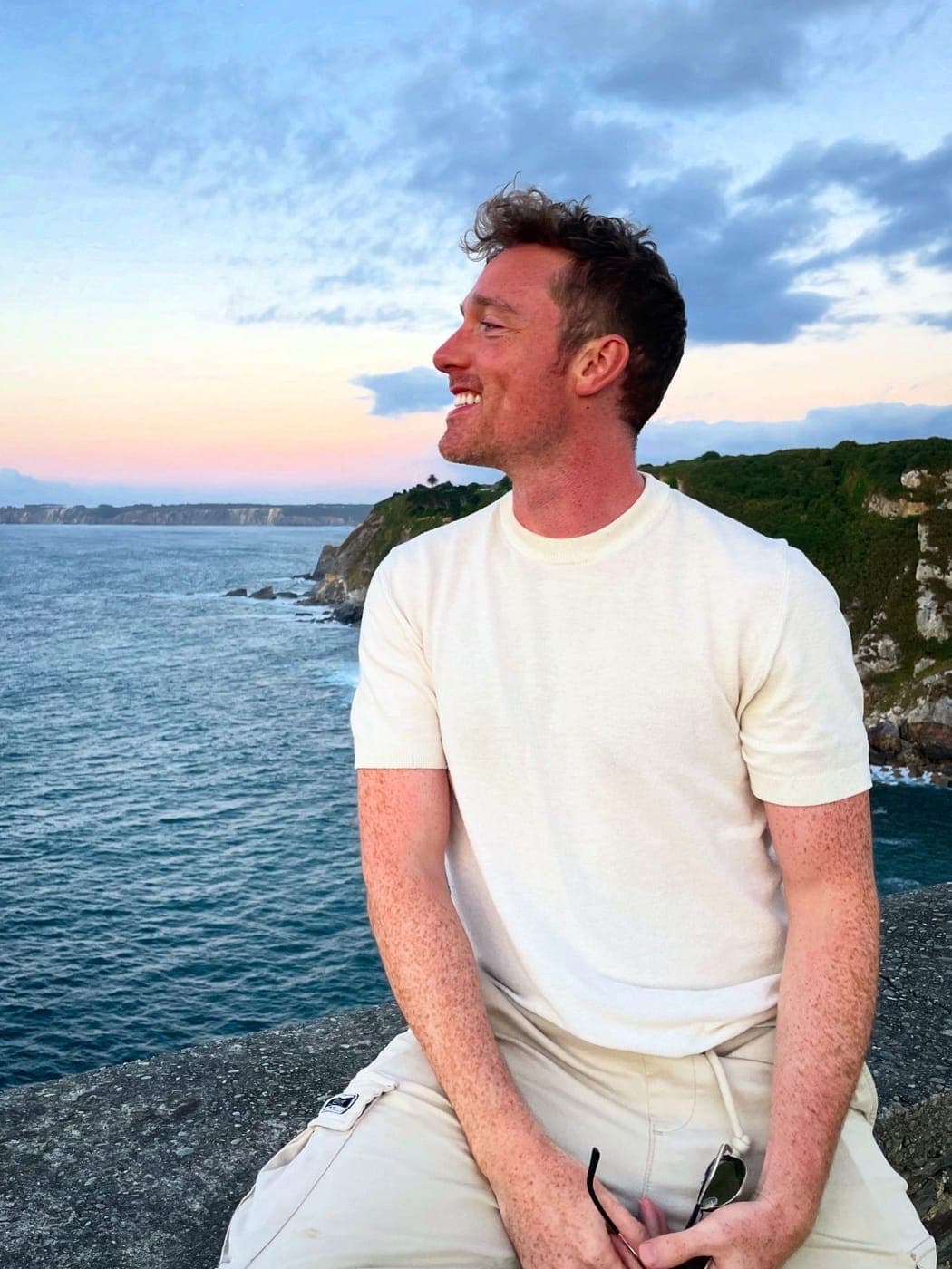 Christopher Adams sitting on a sea wall at dusk, looking out along the cliffs
