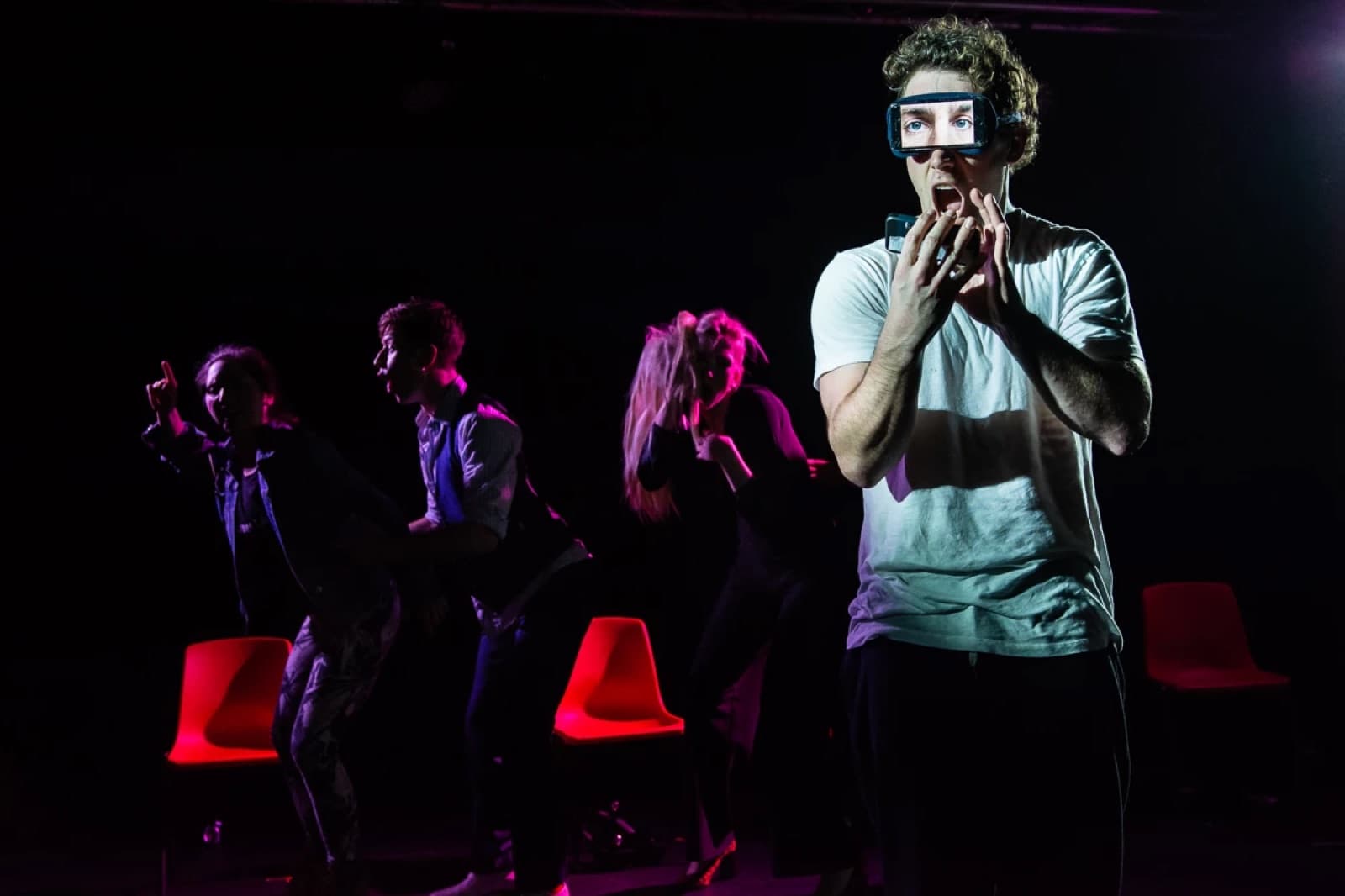 Christopher Adams on stage holding a phone over his eyes showing a pair of eyes